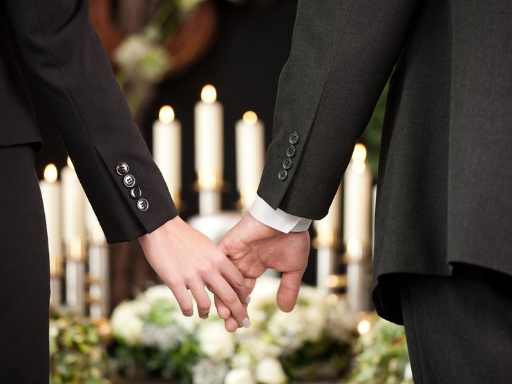 Hände eines Paares halten sich, umgeben von Kerzen und Blumenarrangements, in festlicher Atmosphäre.